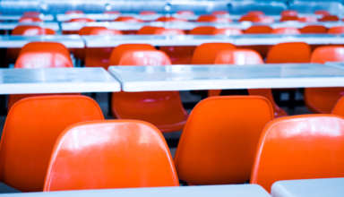 Clean school cafeteria with many empty seats and tables.